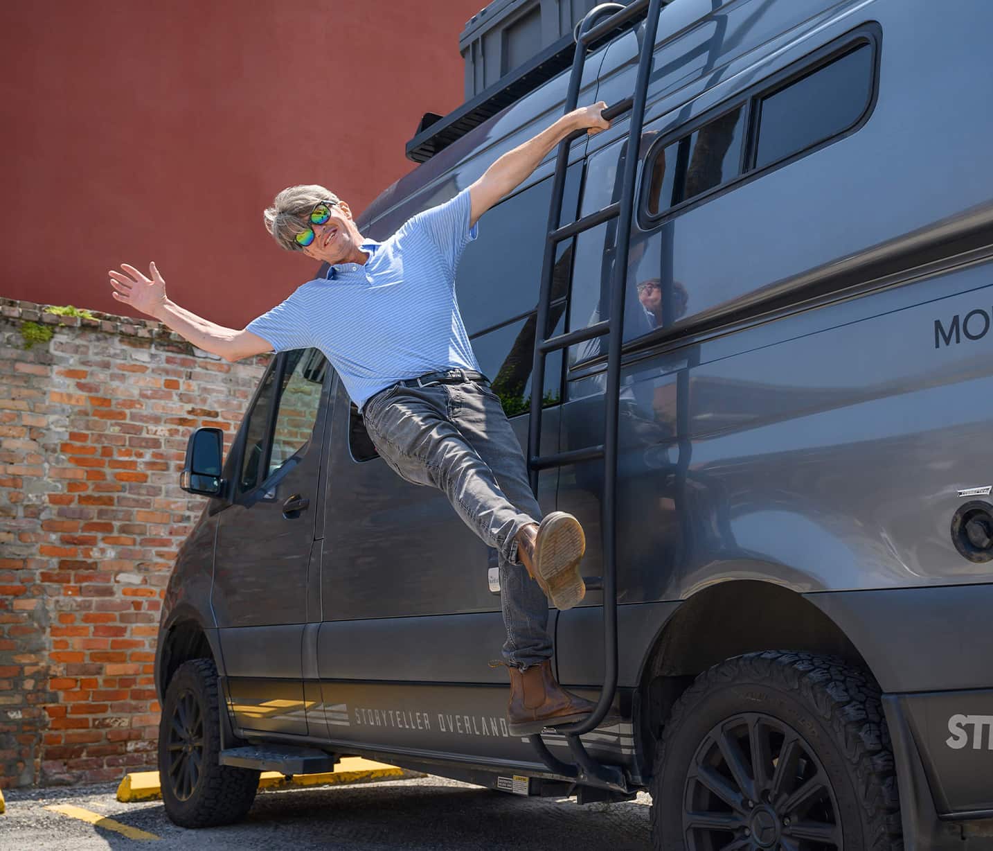 Man hanging from ladder on van.